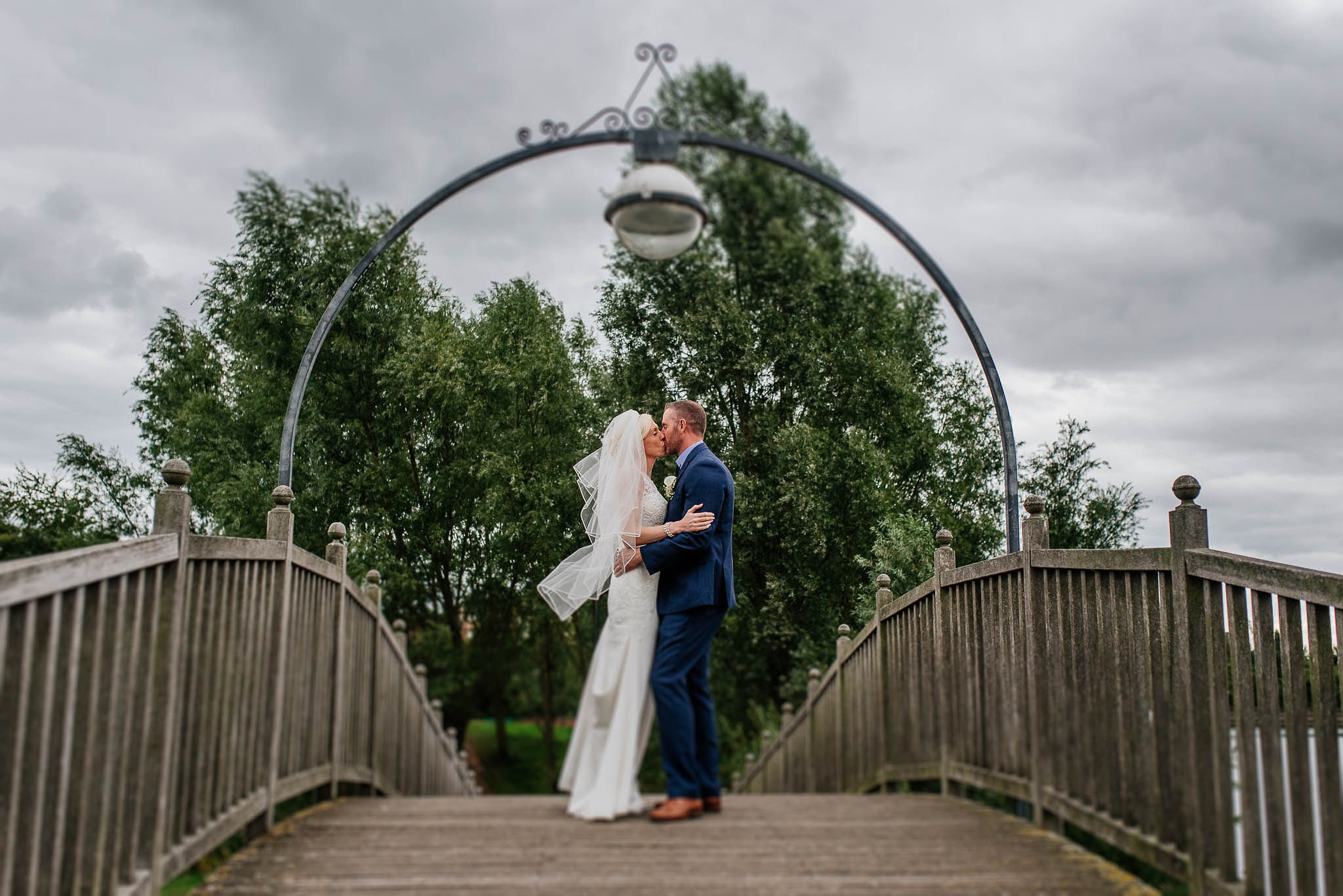 A newly married couple shares a romantic kiss on a picturesque arched bridge in Lakeside, Doncaster on their wedding day.