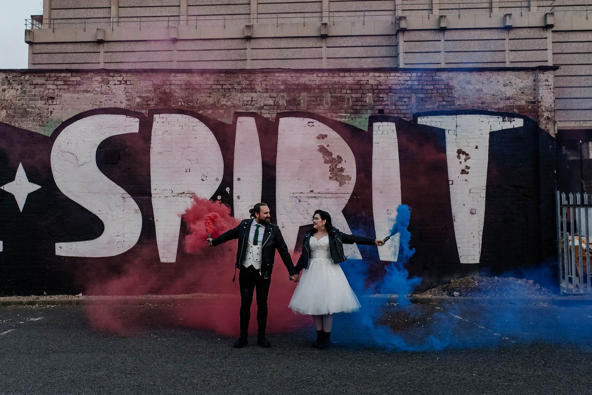 Bride and groom wearing leather jackets and holding smoke bombs