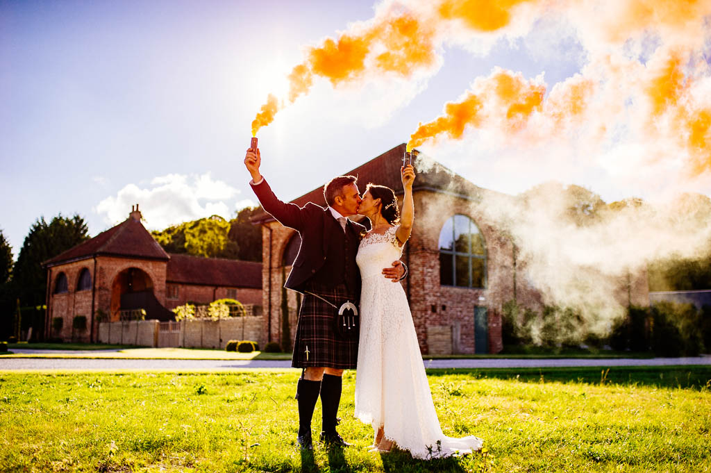 Bride and groom holding smoke bombs for a photograph outside Hazel Gap Barn