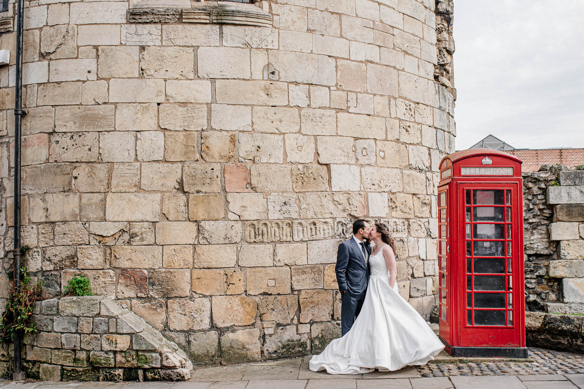 Bride and groom kissing next to a traditional red telephone box.