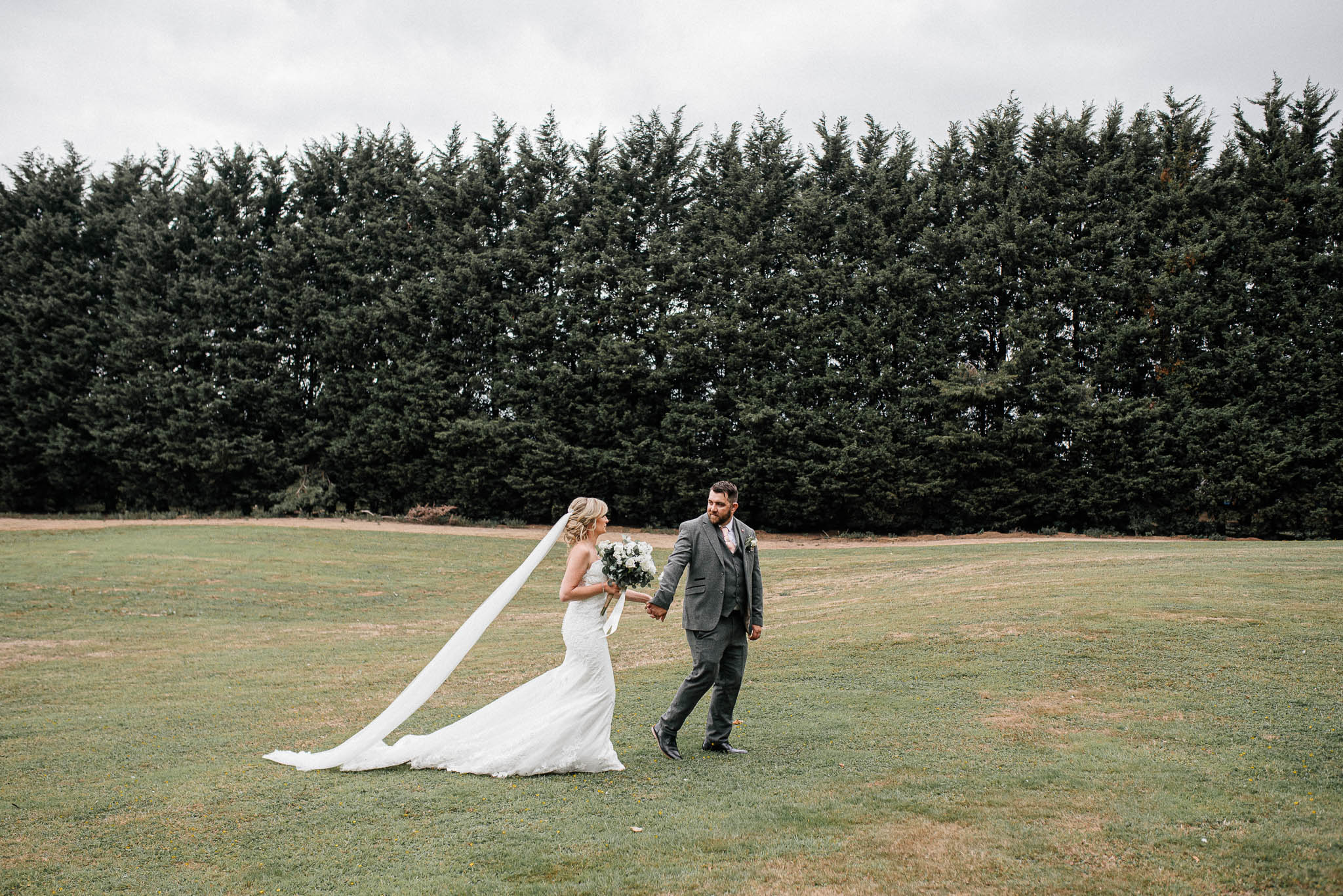 A bride and groom walking on a meadow outside Hellaby Hall Hotel.