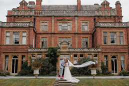 Bride and groom holding hands and kissing outside Rossington Hall wedding venue